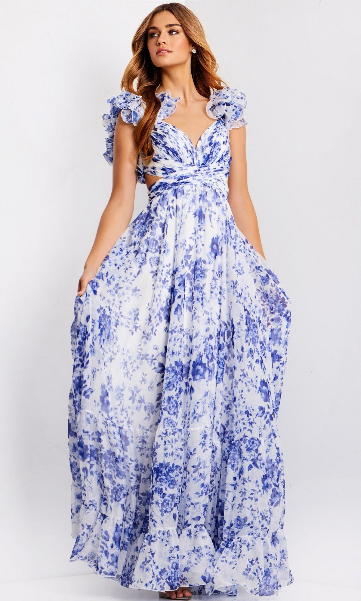 A woman models the Jovani 49143, a ruffled long print prom dress with blue floral patterns, standing against a plain background.